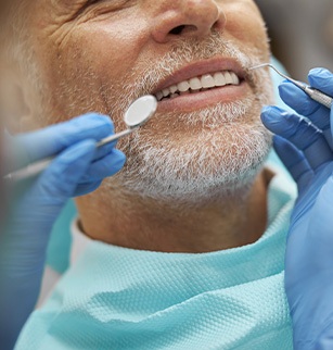 Closeup of blue-gloved hands performing a man’s dental examination