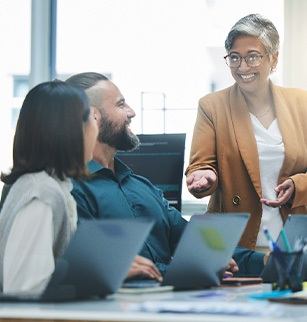 Woman in brown jacket presenting to coworkers over laptops