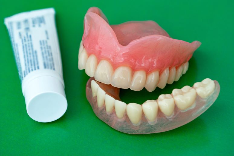 A pair of dentures and a tube of denture adhesive